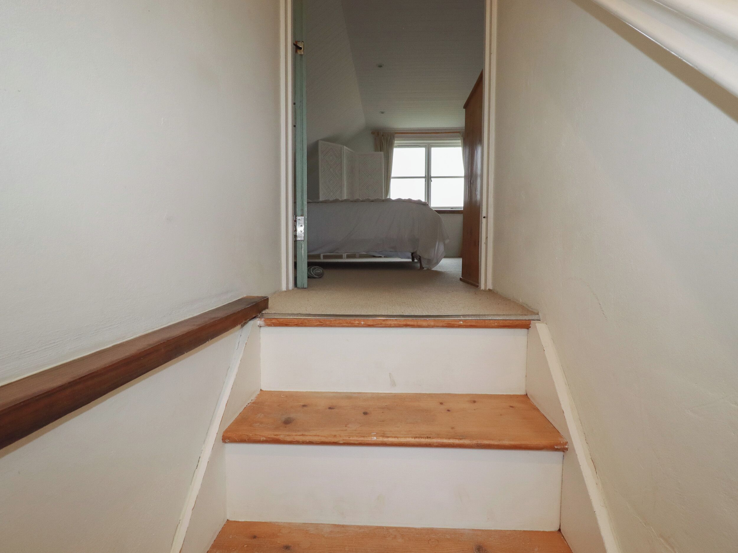 Un escalier étroit avec des marches en bois menant à une chambre.
