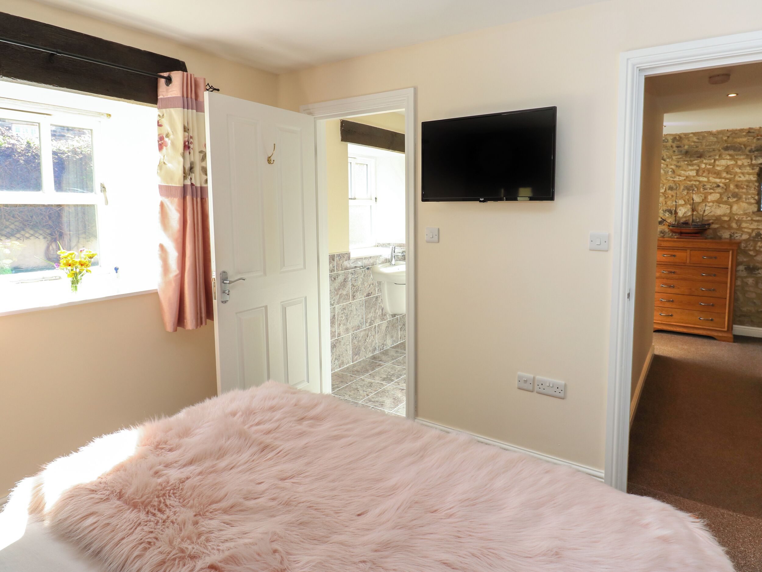 Un dormitorio con cama, televisión en la pared, ventana con cortinas y vistas al exterior.