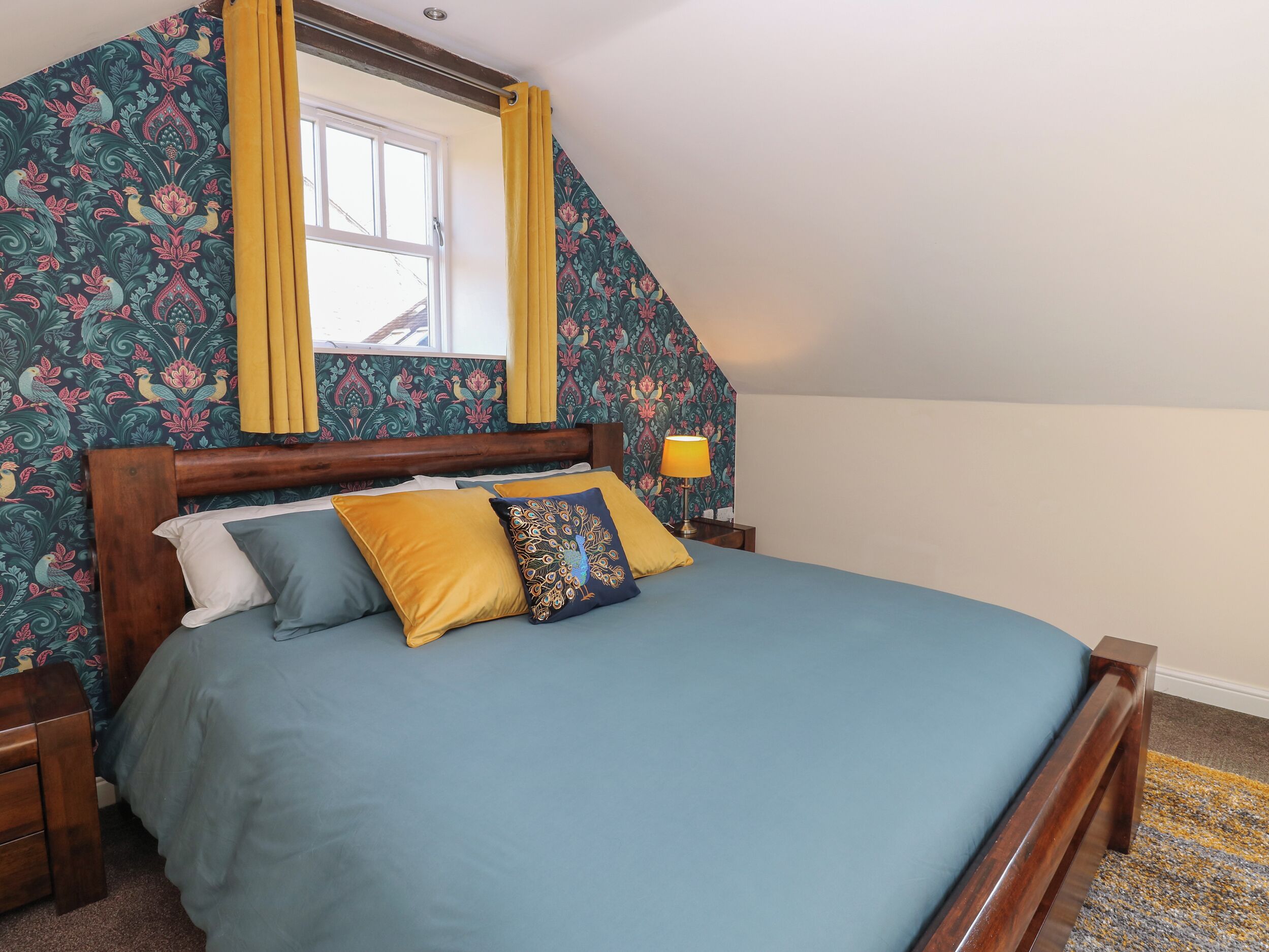 Un dormitorio con una cama de madera, una ventana con cortinas amarillas y un papel tapiz con motivos florales.