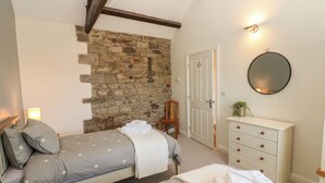 Ein Schlafzimmer mit einer Steinsäule, einem Bett mit grauer Bettwäsche, einem Holzstuhl, einer Kommode und einem runden Spiegel.