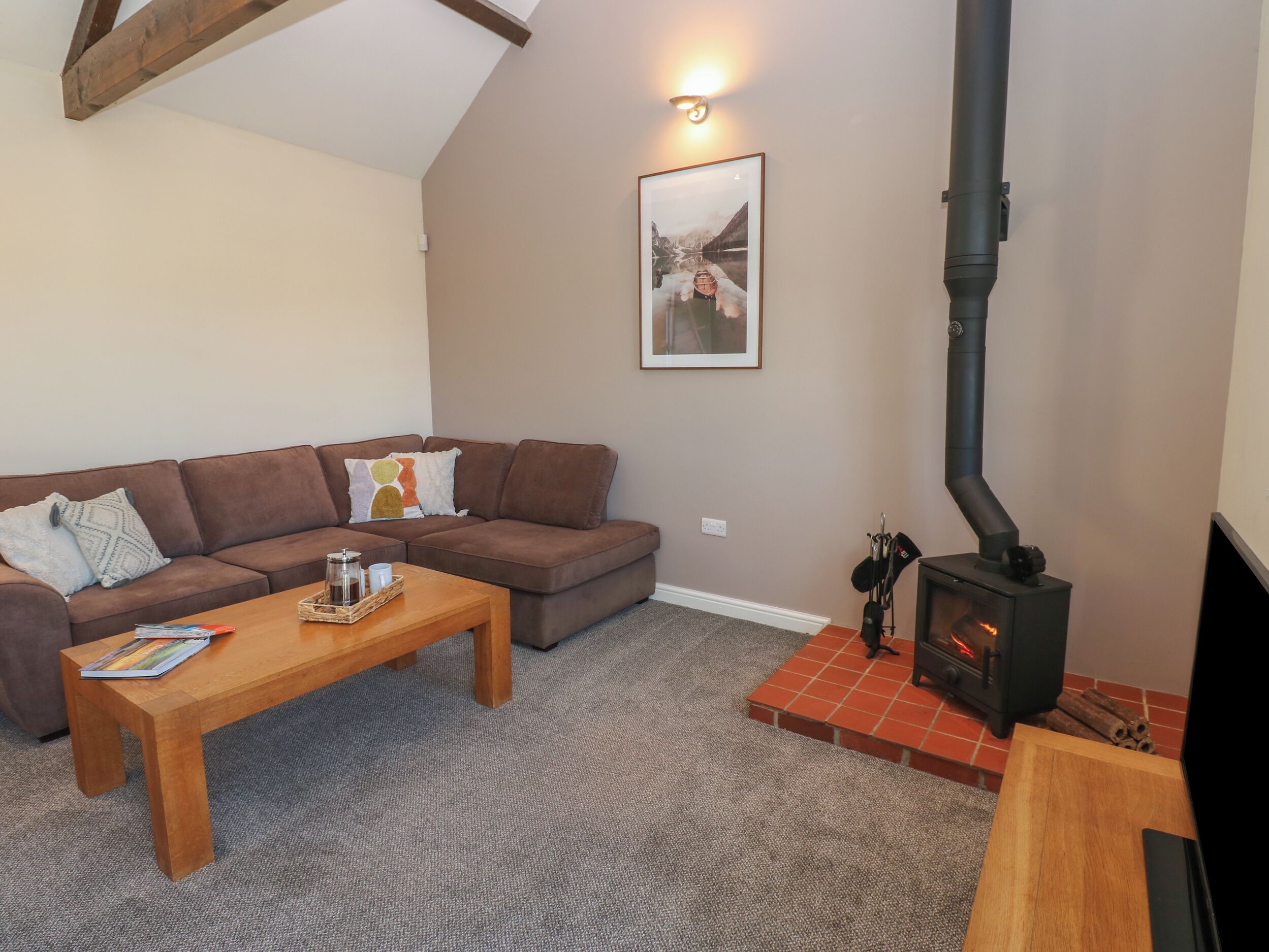 A cozy living room with a brown sofa, a wooden coffee table, a fireplace, and a framed picture on the wall.