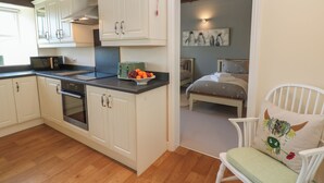 Eine kleine Küche mit weißen Schränken, einer Mikrowelle und einem Toaster. Ein Holzboden und ein weißer Stuhl mit Kissen.