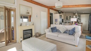 Een ruime woonkamer met een open haard, een bank en een eethoek op de achtergrond.