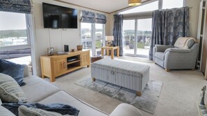 Een ruime woonkamer met een grote flatscreen-tv, een bank, een salontafel en een balkon met uitzicht.