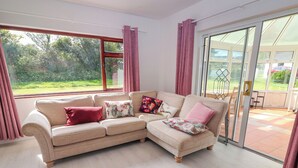 Un sofá seccional color beige con cojines estampados, una almohada roja y una puerta de vidrio que da a un patio exterior.