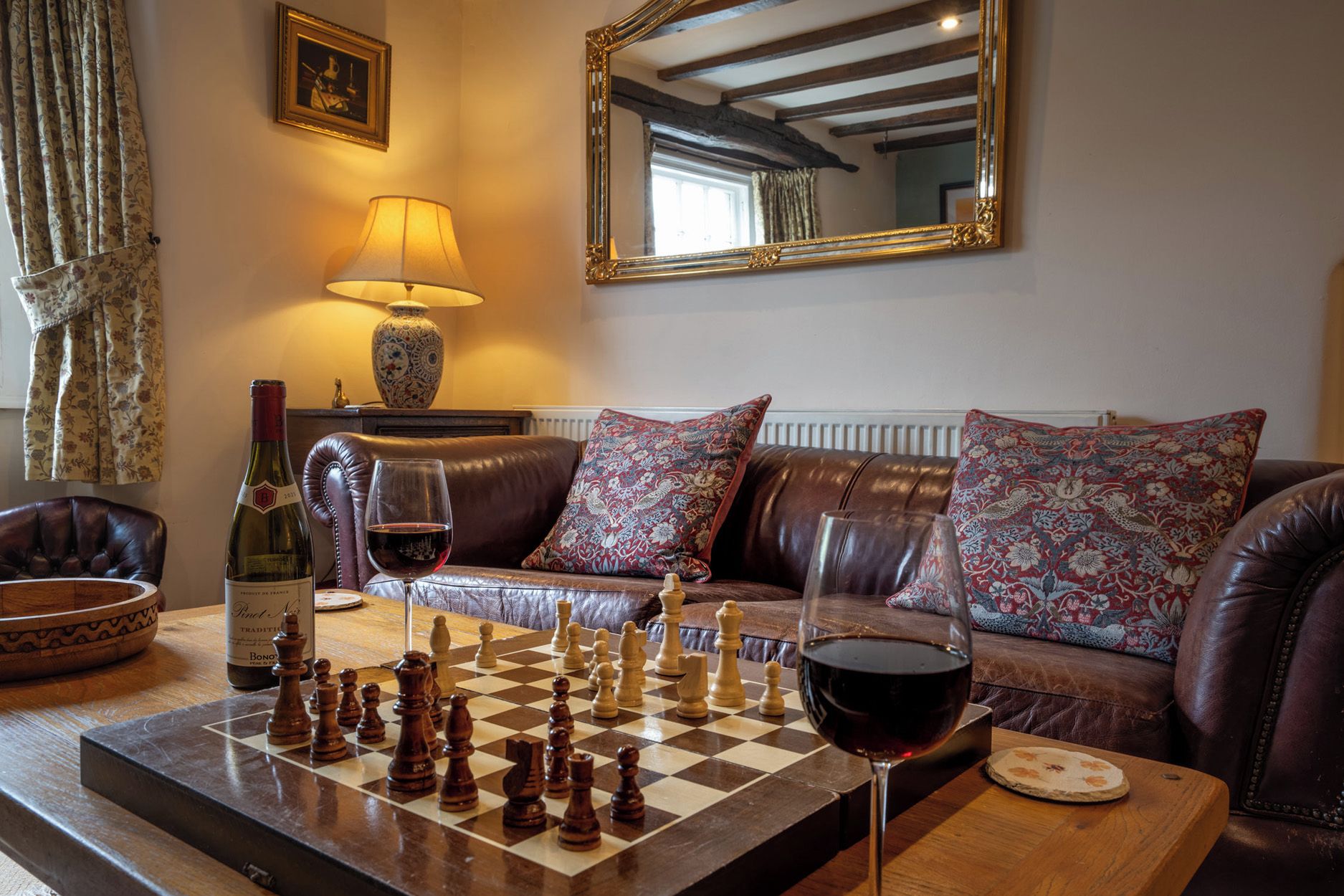 Una sala de estar acogedora con un tablero de ajedrez, una botella de vino y una lámpara.