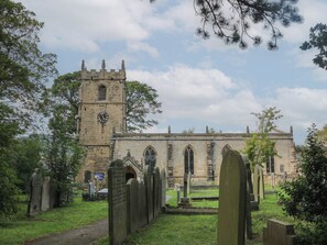 A historic church with a tall tower and a clock, surrounded by a cemetery with headstones. - Buttercup Cottage (Hope Valley)