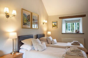 A hotel room with two beds, a window with a view, and wall-mounted lamps.