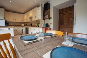 Una cocina moderna con armarios blancos, una mesa de comedor de madera dispuesta con platos, vasos y cubiertos.