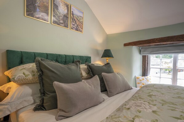 A bedroom with a bed, pillows, a headboard, a lamp, and a window. - Buttercup Cottage (Hope Valley)