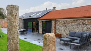 A modern building with stone walls and a red roof, featuring outdoor seating and a patio area.