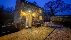 A stone house with a door, two windows, a small porch, and a table with chairs. - School House Cottage (Buxton)
