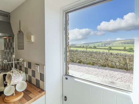 A kitchen with a stone wall view, a hanging rack with cups, and a window with a countryside view.
