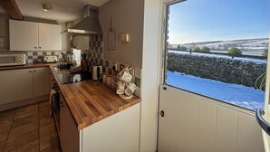 A kitchen with wooden countertops, a microwave, and a view of a snowy landscape through a window. - School House Cottage (Buxton)