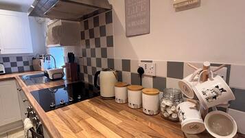 A kitchen with a black stove, white cabinets, a checkered backsplash, and a wall-mounted Accentra air conditioner.