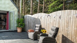 A patio area with wicker furniture, a potted plant, and a wooden fence. - Little Willow (St. Columb Major)