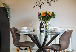 A dining table with two chairs, a bottle of wine, and a vase with flowers.