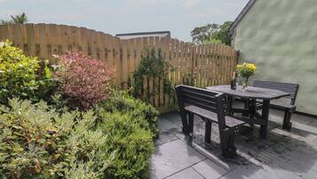 A patio area with a wooden fence, a table with benches, and various plants.