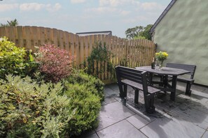 Ein Terrassenbereich mit Holzlattenzaun, Tisch und Bänken sowie verschiedenen Pflanzen.