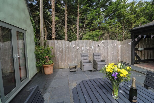 A patio area with a table, two chairs, a potted plant, and a bottle of champagne.