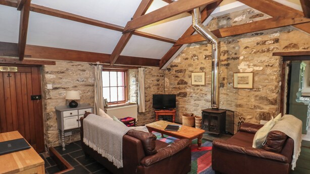 A cozy living room with stone walls, wooden beams, a fireplace, leather sofas, and a television. - Preseli Hills Cottage (Fishguard)