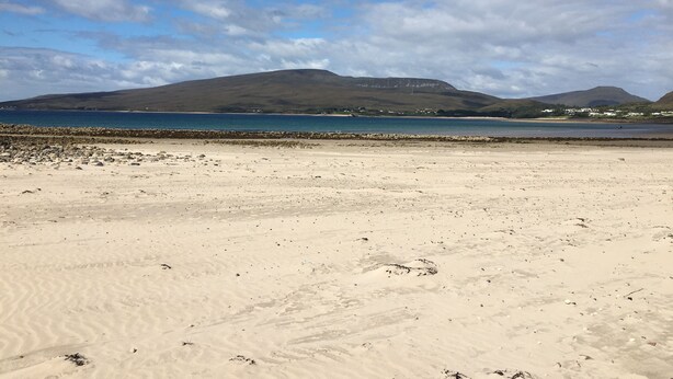 A sandy beach with a rocky breakwater, calm sea, and distant mountains under a partly cloudy sky. - Calvey's Cottage (Newport)