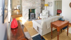 A cozy living room with a stone fireplace, a sofa, a wooden table, and a red vase. - Calvey's Cottage (Newport)