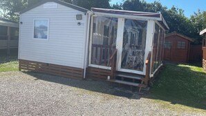 A small, single-story wooden cabin with a porch and a sliding glass door. - Welcome to Lily's Mobile Home (Bernières-sur-Mer)
