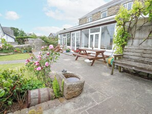 En terrasse med et træbord og bænke, omgivet af stenplantere og en have.