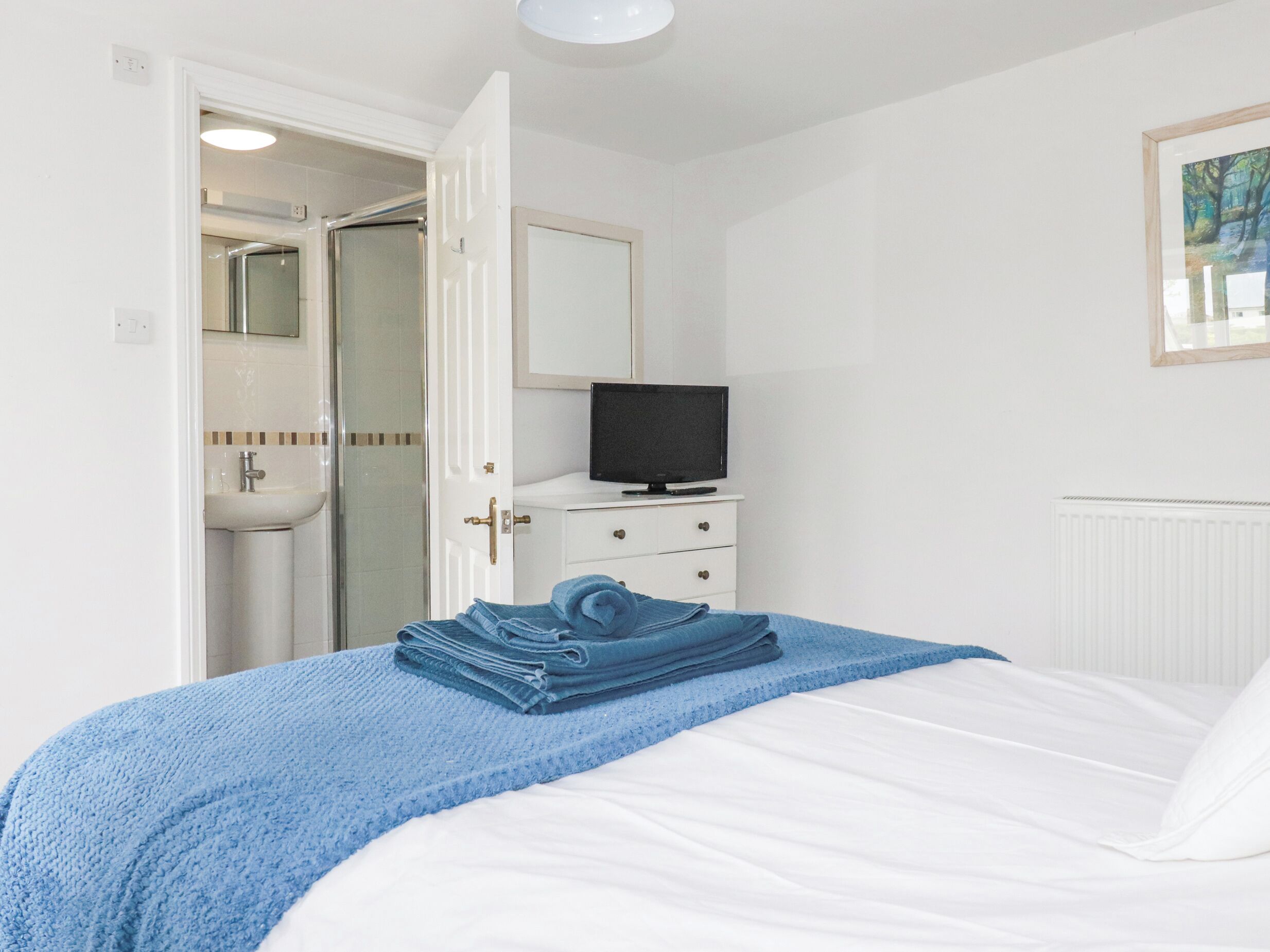 A bedroom with a bed, a TV on a dresser, a bathroom with a mirror and sink, and a door leading to another room.