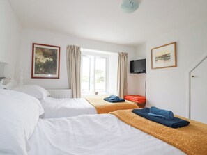 Et hotelværelse med to senge, et vindue med gardiner, et fjernsyn på væggen og et indrammet billede.