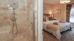 A bathroom with a glass-enclosed shower and a bedroom with a bed, bedside table, and a lamp. - Manor Farm House (Wareham)
