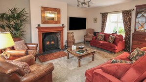 A living room with a fireplace, leather armchairs, a red sofa, a coffee table, and a television mounted on the wall. - Manor Farm House (Wareham)