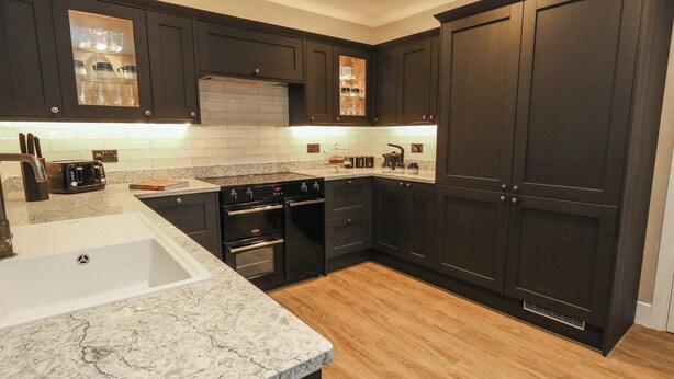 A modern kitchen with dark cabinetry, a white sink, and a marble countertop. - Manor Farm House (Wareham)