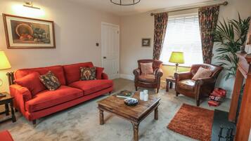 A living room with a red sofa, two leather armchairs, a wooden coffee table, and a large window with curtains.