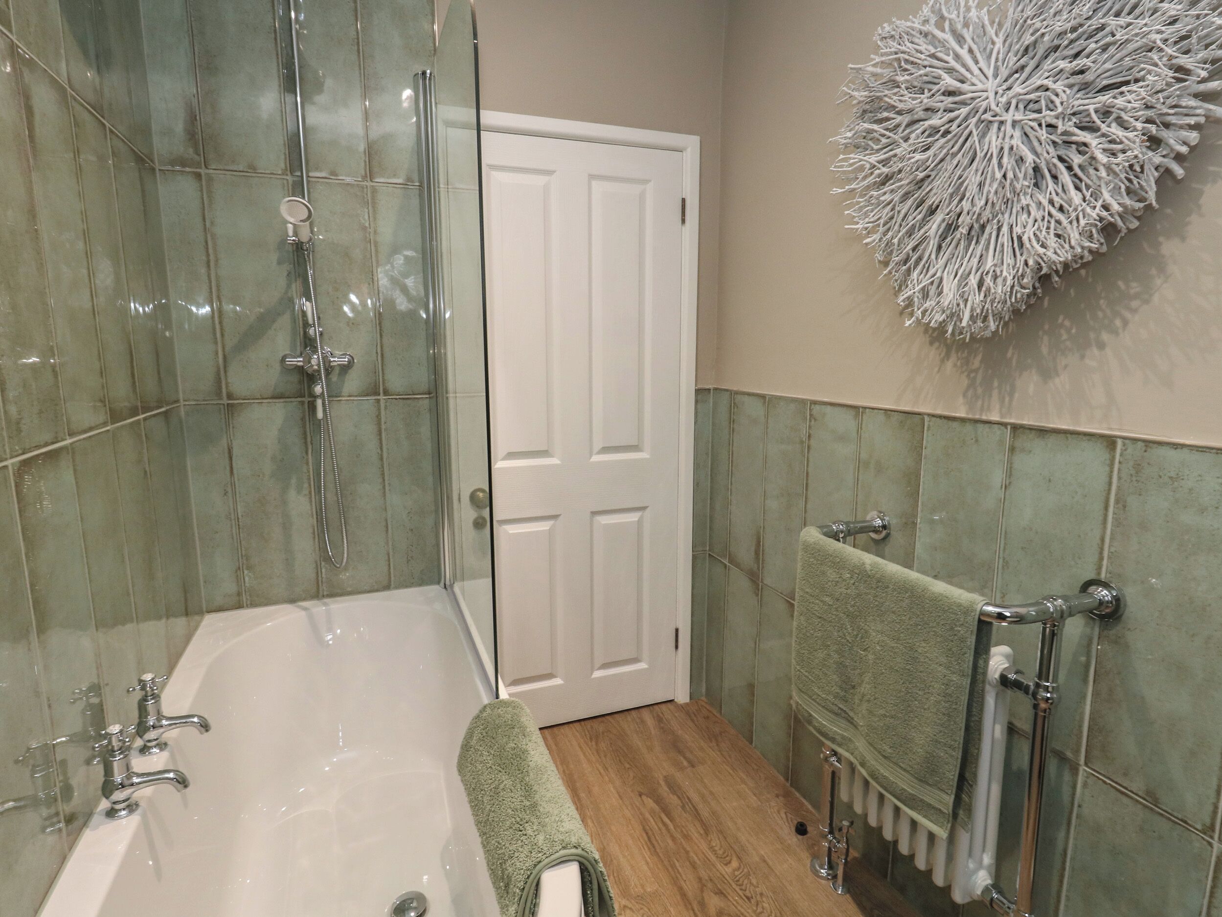A bathroom with a glass-enclosed shower, a white bathtub, and a green towel.