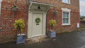 A brick house with a white door labeled "Manor Farm House," two potted plants, and a small garden area. - Manor Farm House (Wareham)