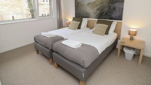 Una cama doble con dos almohadas, una mesita de noche con lámpara, una ventana con cortinas y un cuadro en la pared.