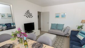 Una sala de estar moderna con comedor, televisor de pantalla plana y sofá con cojines color turquesa.