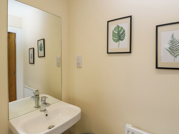 Un baño con lavamanos blanco, un espejo e impresiones botánicas enmarcadas en la pared.