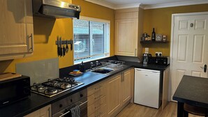 A compact kitchen with a gas stove, a dishwasher, wooden cabinets, and a window with blinds. - 22 Two Little Ducks (Lynton)