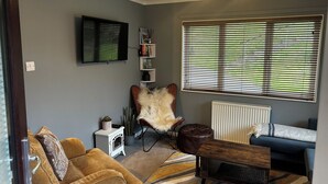 A living room with a sofa, armchair, small table, bookshelf, and a large window with blinds. - 22 Two Little Ducks (Lynton)