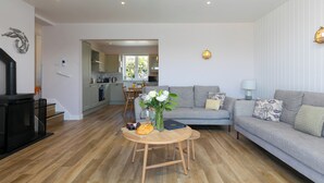 Un salon moderne avec un canapé gris, une table basse en bois et une cuisine en arrière-plan.