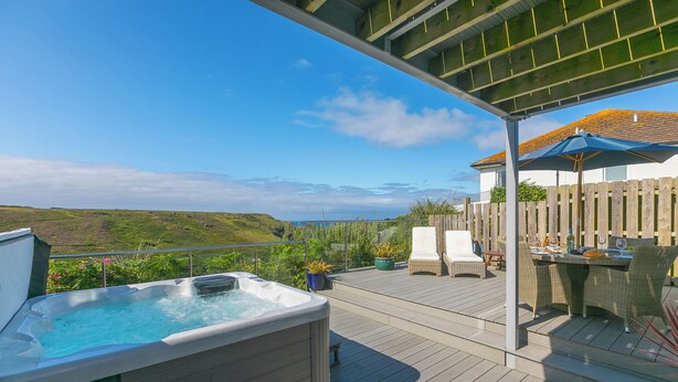 Un bain à remous sur une terrasse en bois, avec vue sur l’océan et les collines.