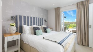 Une chambre à coucher avec un grand lit, une table de chevet, une lampe et une vue sur l’extérieur.