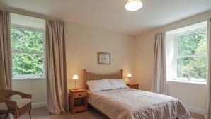 Une chambre à coucher comprenant un lit, deux tables de chevet, une chaise et de grandes fenêtres avec des rideaux.