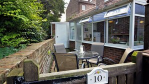 A patio with a table and chairs, a wooden fence with a sign, and a building with windows and a door. - New Tower House- 10 Pear Tree Court (York)