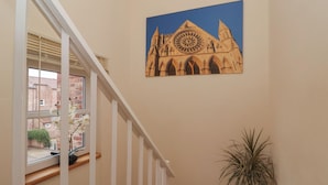 A staircase with a white railing, a window with blinds, a potted plant, and a framed picture of a cathedral on the wall. - New Tower House- 10 Pear Tree Court (York)