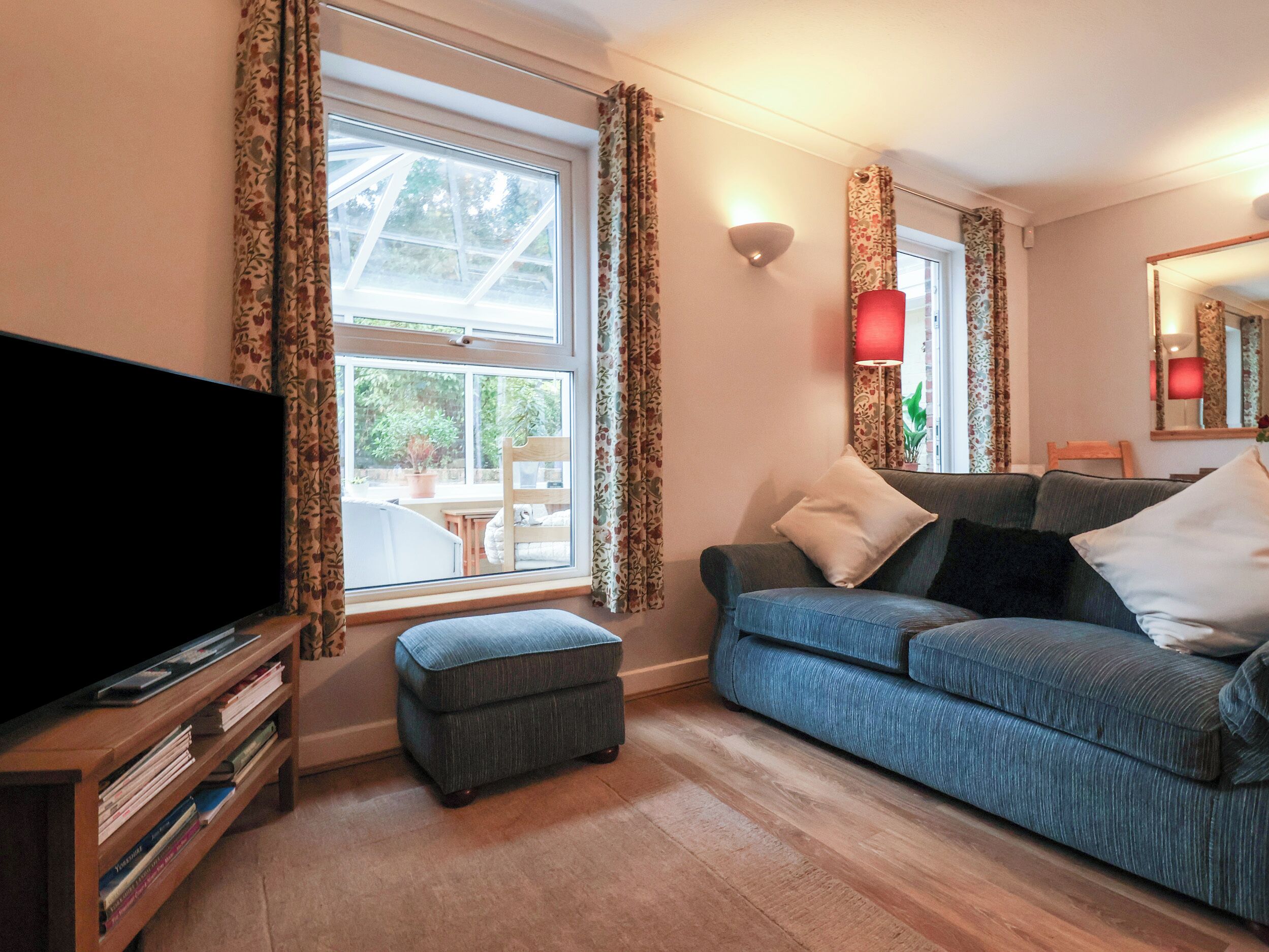 A living room with a sofa, ottoman, and a flat-screen TV on a wooden stand.