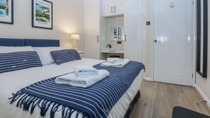 Une chambre d’hôtel avec un grand lit, une table de chevet avec une lampe, une armoire et une porte ornée d’une ancre.